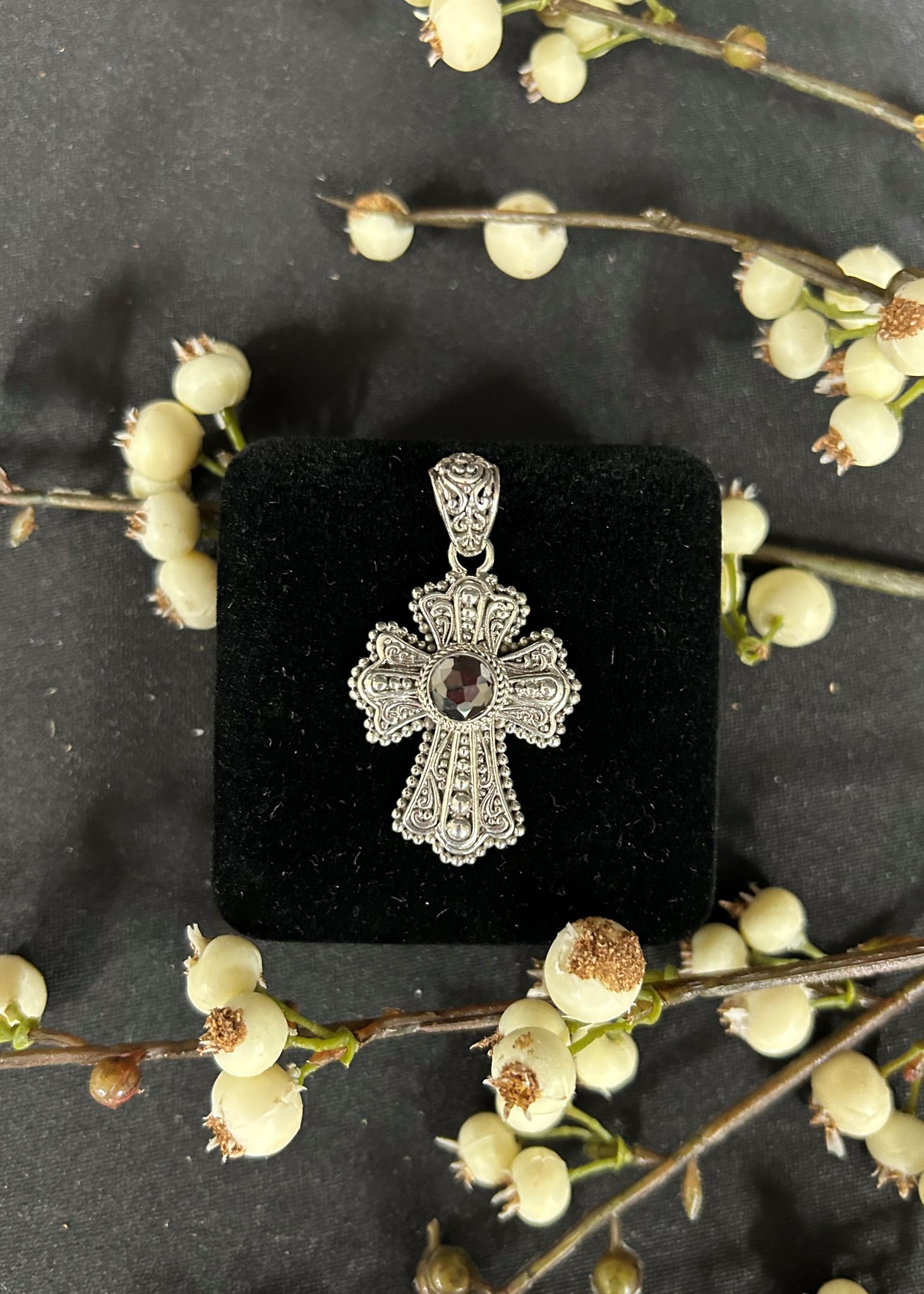 Silver cross pendant with a gemstone on a black display box