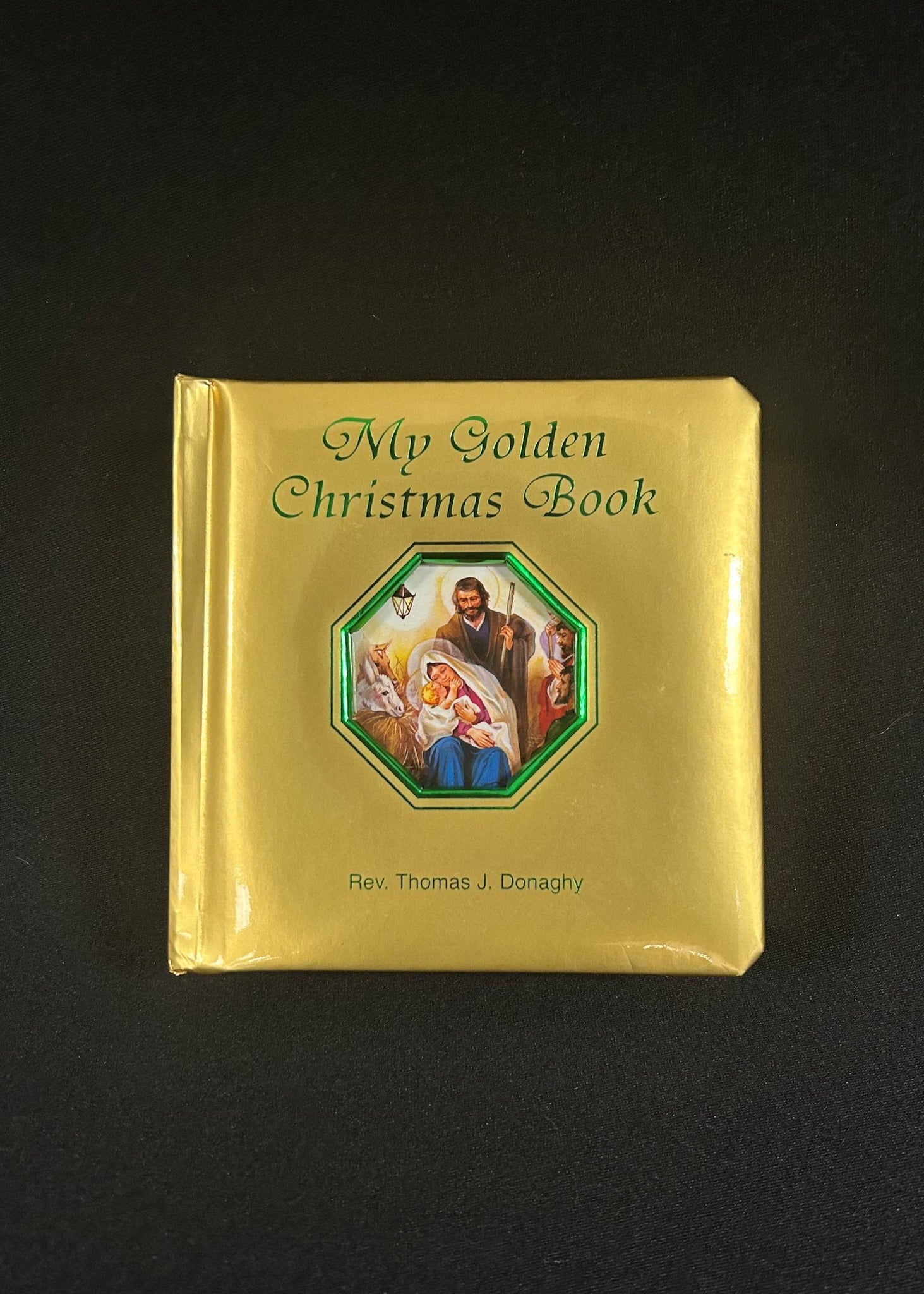 A board book with a golden cover featuring an illustration of the nativity scene, titled 'My Golden Christmas Book' by Rev. Thomas J.