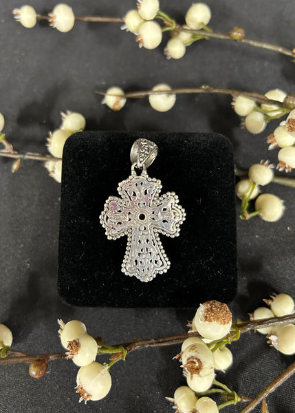 Silver cross pendant on a black display stand with floral background
