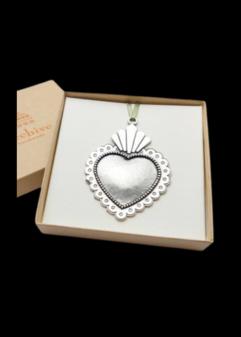 A pewter ornament in the shape of a sacred heart, with intricate detailing, housed in a gift box with a brand tag visible.