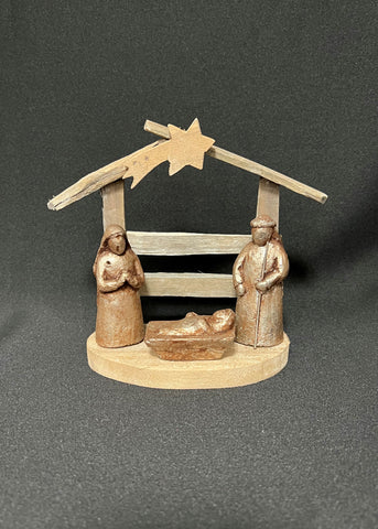 A handcrafted wooden nativity set featuring figures representing the mother and child with a backdrop of a small house and a star.