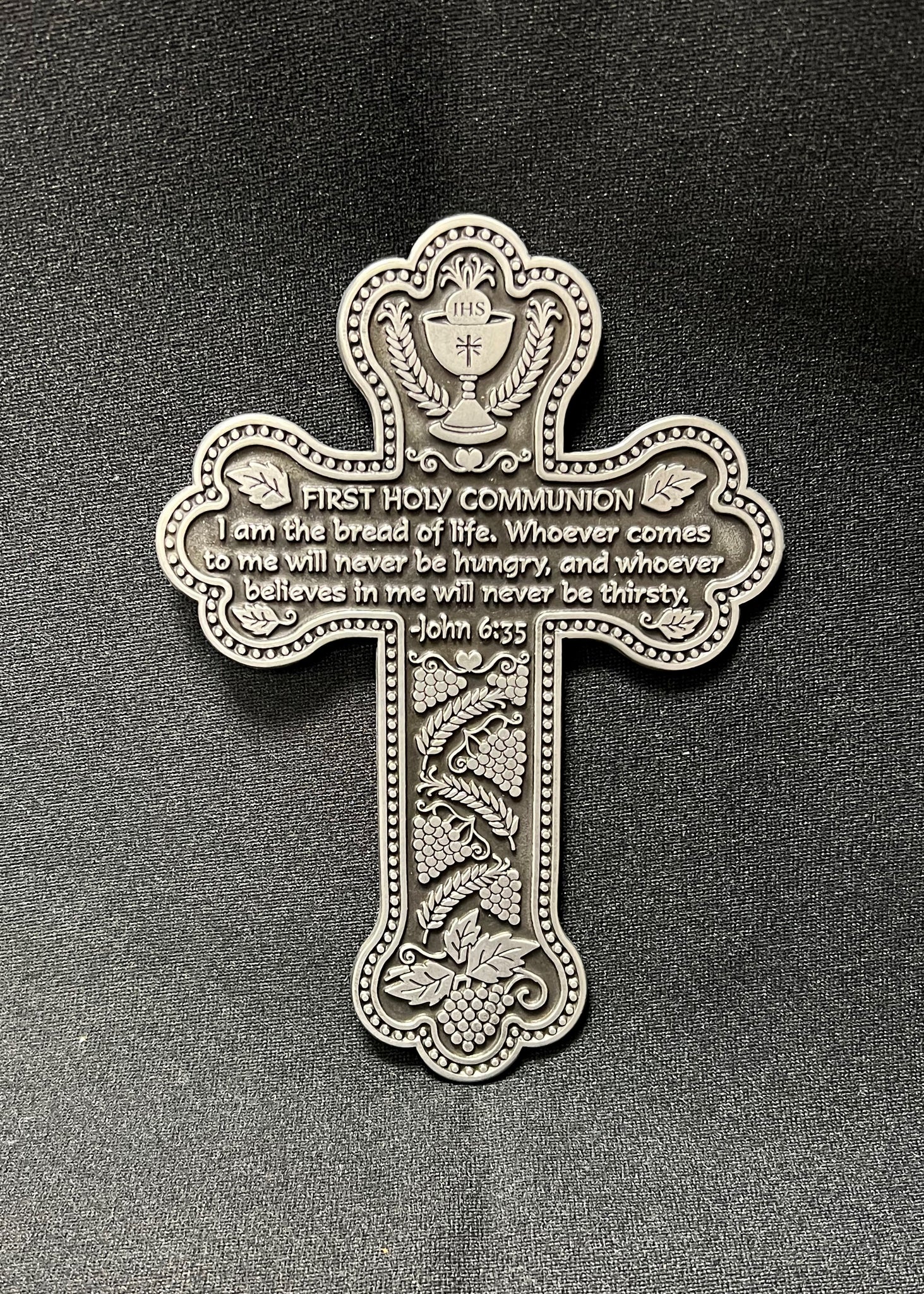 A silver pewter First Holy Communion message cross with biblical verses inscribed, hand-polished and brightly finished, including a hanging metal notch.